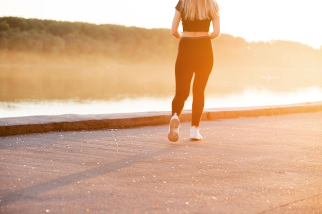 Una mujer con una figura musculosa delgada corre con ropa deportiva negra y zapatillas blancas.