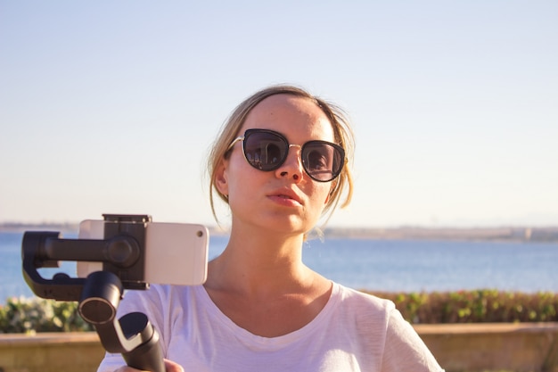 Foto mujer filmando el atardecer en un viaje, video blogger haciendo video con cardán y teléfono móvil