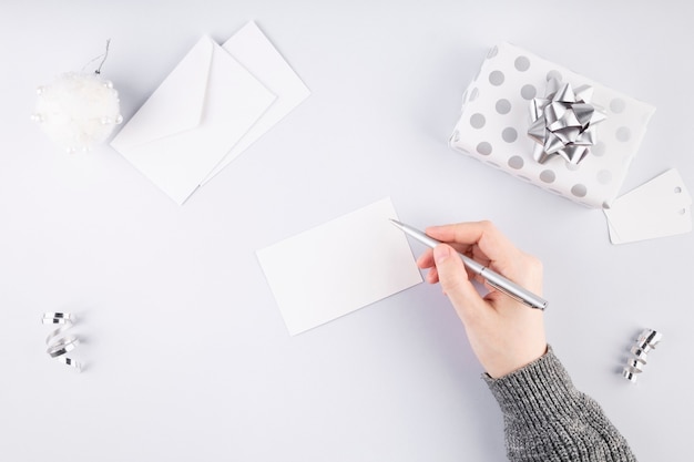 Mujer firma tarjeta para regalo en envases plateados. Concepto de preparación para las vacaciones. Vista superior. Copia espacio