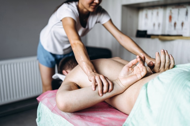 Una mujer fisioterapeuta haciendo masaje de espalda para un hombre en el consultorio médico. Primer plano de las manos que ponen las manos del paciente a la espalda