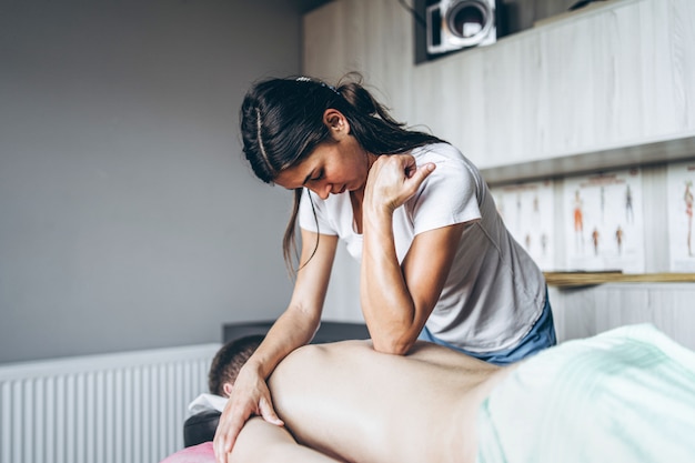 Una mujer fisioterapeuta haciendo masaje de espalda para un hombre en el consultorio médico