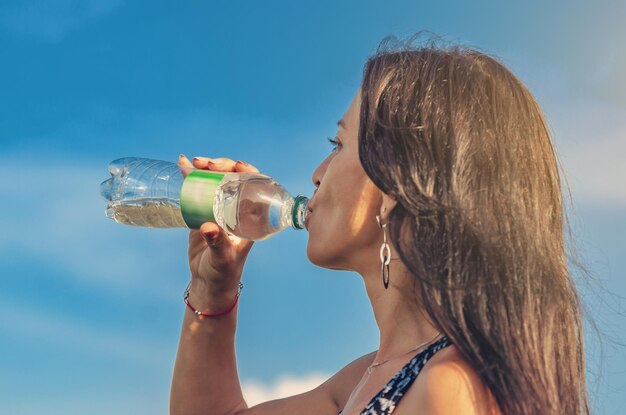 Foto mujer de fitness bebiendo agua de la botella después del entrenamiento de pie en la naturaleza