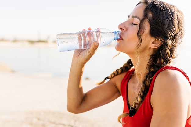 Foto mujer fitness bebiendo agua de botella después de la sesión de entrenamiento por la mañana junto al mar