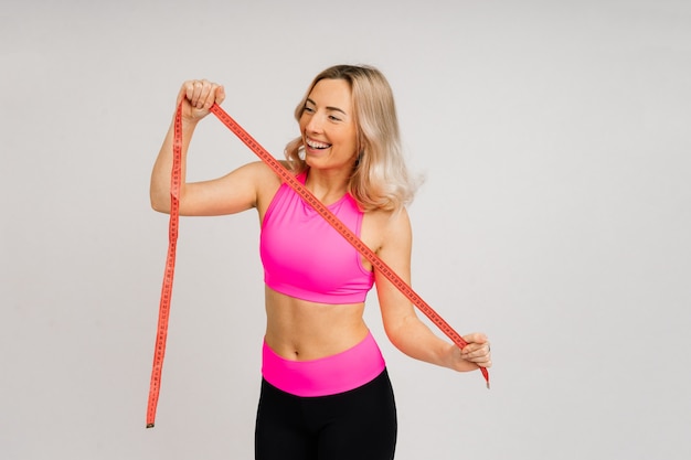 Mujer fitness con cinta métrica mostrando su cintura sobre un fondo de estudio