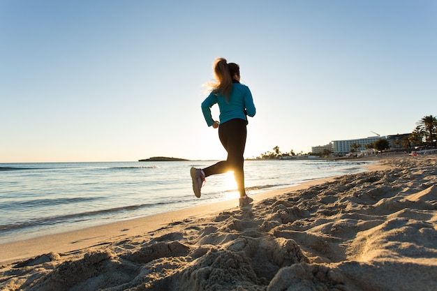 Mujer fitness corriendo por el océano al atardecer.