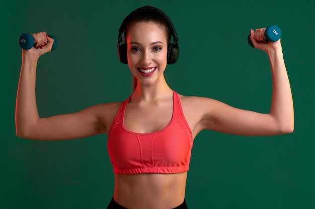 Mujer fitness con cuerpo fuerte haciendo ejercicio con pesas en el interior y escuchar música en auriculares