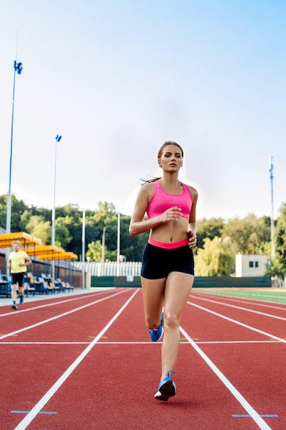 Mujer de fitness deportivo trotar en pista roja en el estadio de entrenamiento de verano al aire libre en ...