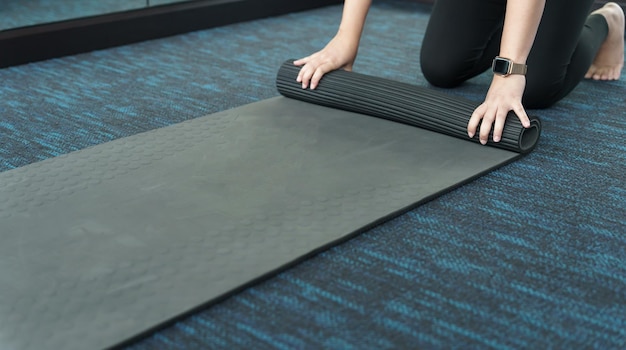 Mujer de fitness doblando alfombra de ejercicio antes de hacer ejercicio en el estudio de yoga rodando alfombra de yoga después de entrenar estilo de vida saludable