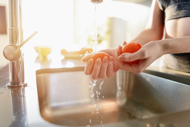 Mujer fitness enjuaga tomate fresco en el fregadero