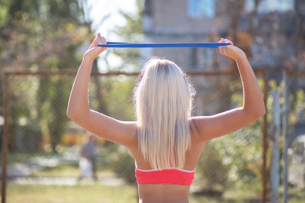 Mujer fitness esbelta haciendo ejercicios de manos con goma elástica al aire libre por la mañana. Espacio vacio