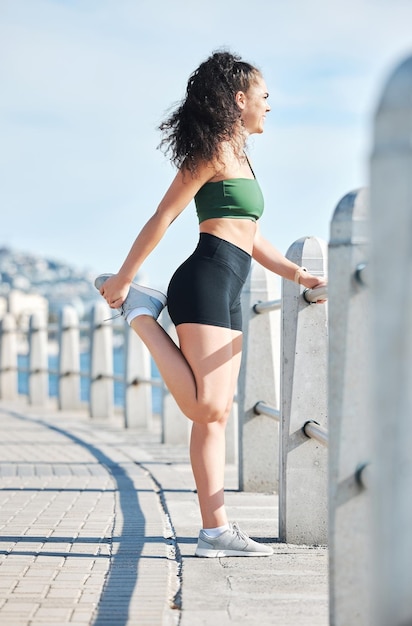 Mujer fitness y estiramiento de piernas para correr ejercicio o entrenamiento cardiovascular en la playa en Ciudad del Cabo Corredora activa en preparación de estiramiento de piernas para calentar ejercicio o entrenamiento en la naturaleza