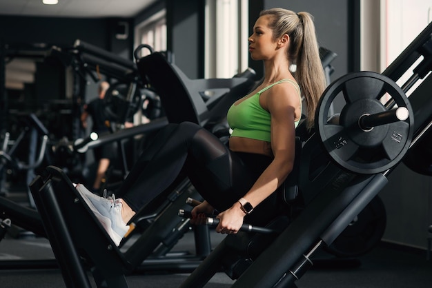 Foto mujer de fitness haciendo cuclillas en la máquina de hack en un gimnasio moderno