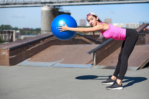 Mujer fitness haciendo ejercicios de estiramiento con fit ball en el fondo urbano de la ciudad