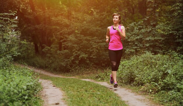 Mujer fitness joven corriendo en la pista forestal de la mañana. Vivir en forma saludable.