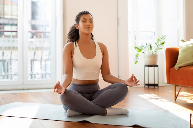 Una mujer de fitness pacífica meditando en un tapete de yoga sentada en el interior