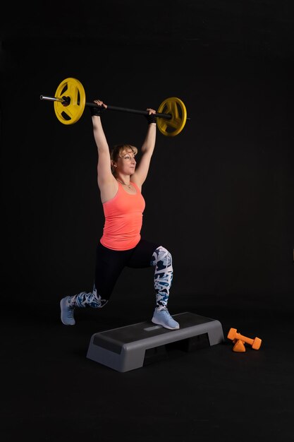 Mujer fitness en una plataforma escalonada con una barra con mancuernas Practica deportes en un negro