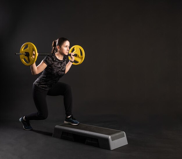 Mujer fitness en una plataforma escalonada con panqueques amarillos con barra en la barra hace ejercicios