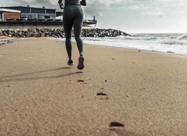 Mujer fitness en ropa deportiva corriendo en la playa dejando huellas en la arena