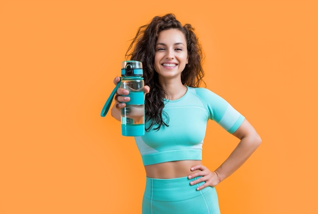 mujer de fitness sonriente con una botella de agua deportiva en el estudio mujer de fitness sostiene una botella de agua deportiva aislada en fondo amarillo fitness y deporte