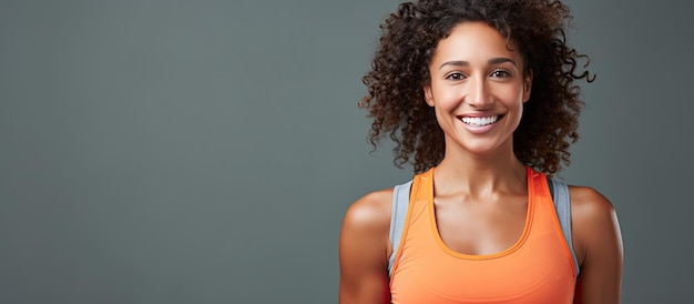 Una mujer fitness sonriente en ropa deportiva posa para un retrato después de un entrenamiento en el gimnasio aislado en un fondo gris