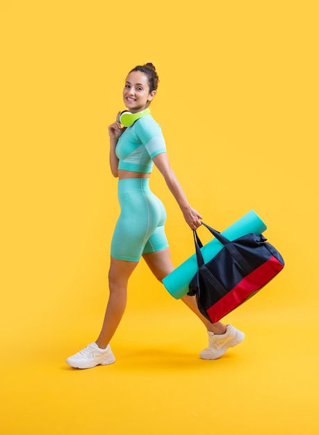 mujer fitness sonrisa en ropa deportiva caminar con bolsa de deporte en estudio mujer fitness en ropa deportiva de entrenamiento aislada sobre fondo amarillo fitness y ropa deportiva