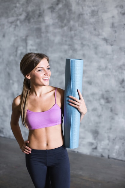 Mujer fitness sosteniendo estera de yoga en el interior.