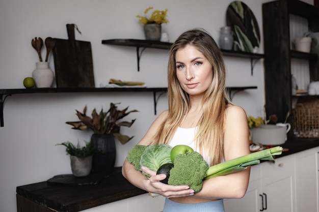 Una mujer fitness tiene un lleno de verduras frescas crudas