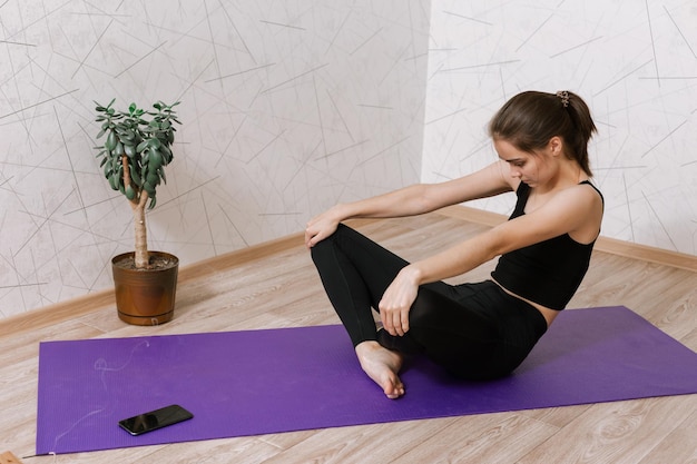 mujer flexible en ropa deportiva sentada en una alfombra en pose Easy Sit y haciendo yoga en la habitación en casa