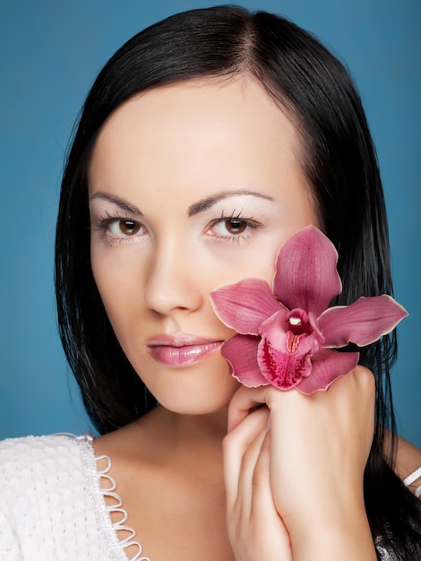 Mujer con flor de orquídea sobre fondo azul.