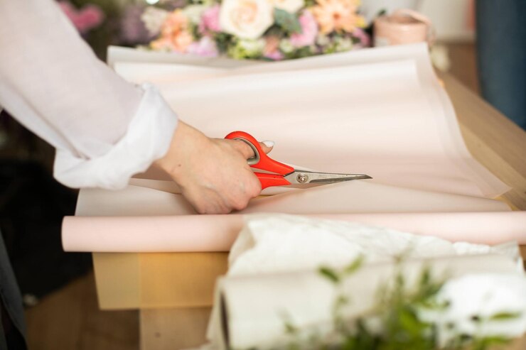 mujer florista cortando papel en la mesa con plantas