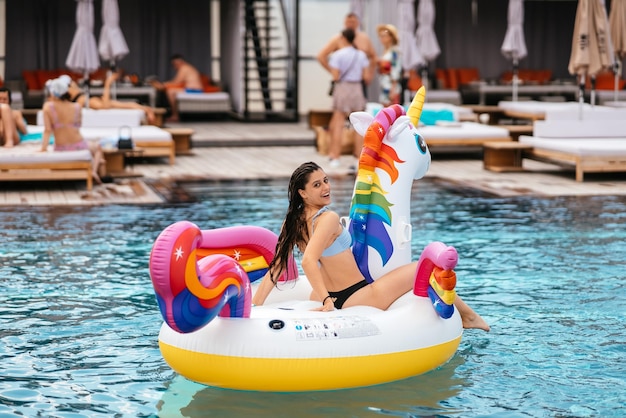 Mujer en flotador inflable de colchón de juguete de unicornio en la piscina