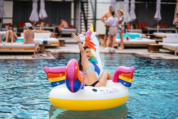 Mujer en flotador inflable de colchón de juguete de unicornio en la piscina