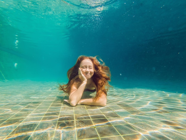 Mujer en el fondo de la piscina, se sumerge bajo el agua.