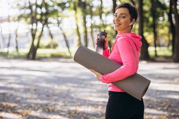 Foto mujer en forma bebiendo agua en el parque y sosteniendo estera de yoga