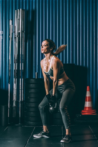 Mujer en forma entrenando levantando pesas rusas en el gimnasio