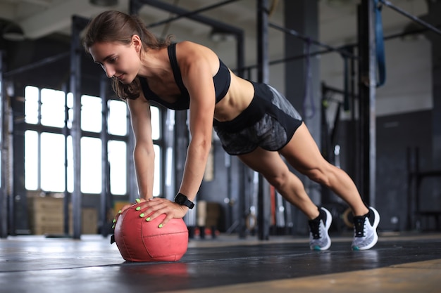 Mujer en forma y musculosa haciendo ejercicio con balón medicinal en el gimnasio.