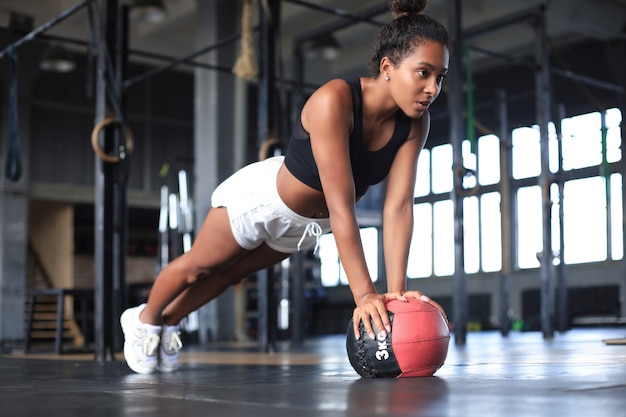 Mujer en forma y musculosa haciendo ejercicio con balón medicinal en el gimnasio.
