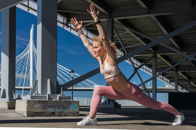 mujer en forma en la parte superior y leggings entra para hacer deporte debajo del puente urbano en un día soleado