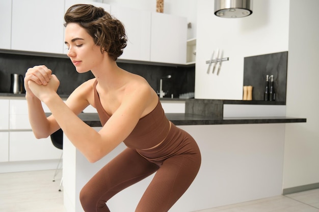 Mujer en forma en ropa deportiva está haciendo ejercicios en cuclillas en casa ejercicio físico en interiores