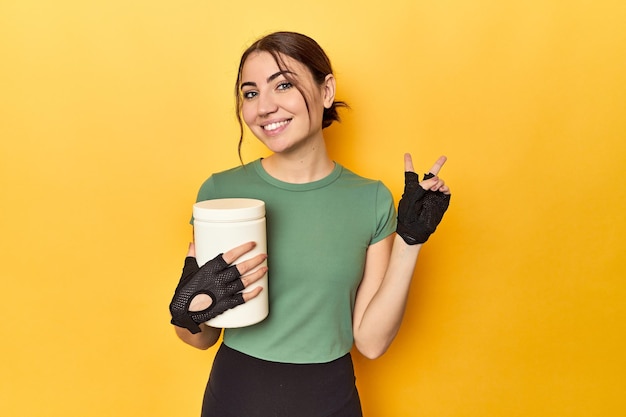 Foto mujer en forma sosteniendo un batido de proteínas alegre y despreocupada mostrando un símbolo de paz con los dedos