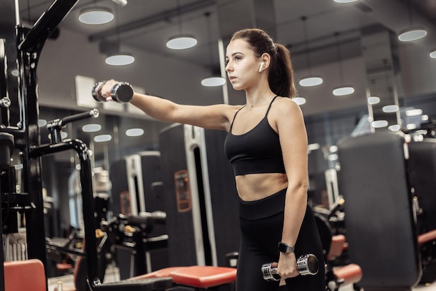 Una mujer en forma trabaja con pesas livianas en el moderno gimnasio Entrenamiento muscular del hombro Estilo de vida saludable