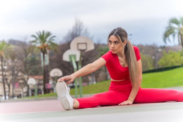 Mujer en forma con traje rojo que se extiende en una cancha de baloncesto fitness y concepto activo saludable