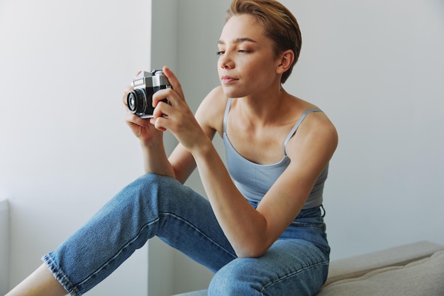 Mujer fotógrafa disparando en el estudio con una cámara de película antigua en casa en un sofá retrato fondo blanco espacio de copia libre fotógrafo independiente