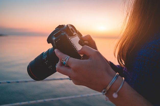 Mujer fotógrafa sostiene la cámara réflex digital durante la toma de fotos al mar