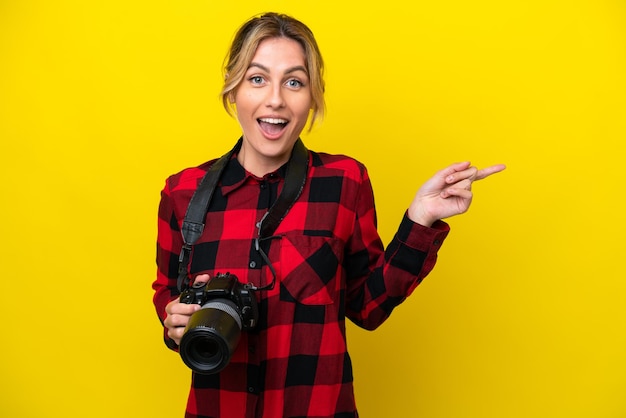 Mujer fotógrafa uruguaya aislada de fondo amarillo sorprendida y apuntando hacia el lado