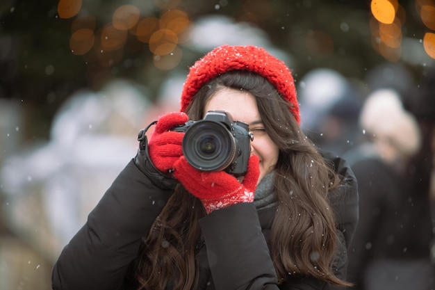 mujer fotógrafo con cámara profesional disparando al aire libre en invierno árbol de Navidad en el fondo