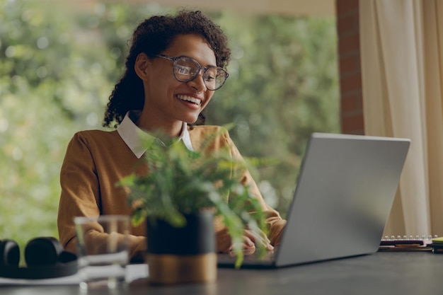 Mujer freelance trabajando con computadora portátil remotamente mientras está sentada cerca de la ventana en el concepto de trabajo a distancia en casa