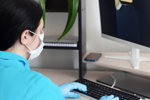 Una mujer frente a una computadora con una mascarilla protectora y guantes protectores Un trabajador médico