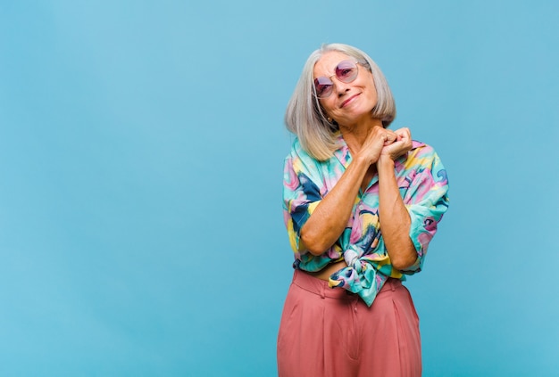 Mujer fresca de mediana edad que se siente enamorada y se ve linda, adorable y feliz, sonriendo románticamente con las manos al lado de la cara