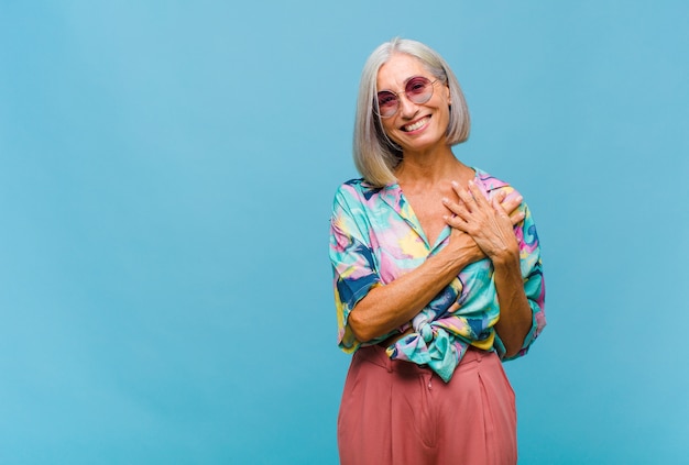 Mujer fresca de mediana edad que se siente romántica, feliz y enamorada, sonriendo alegremente y tomados de la mano cerca del corazón